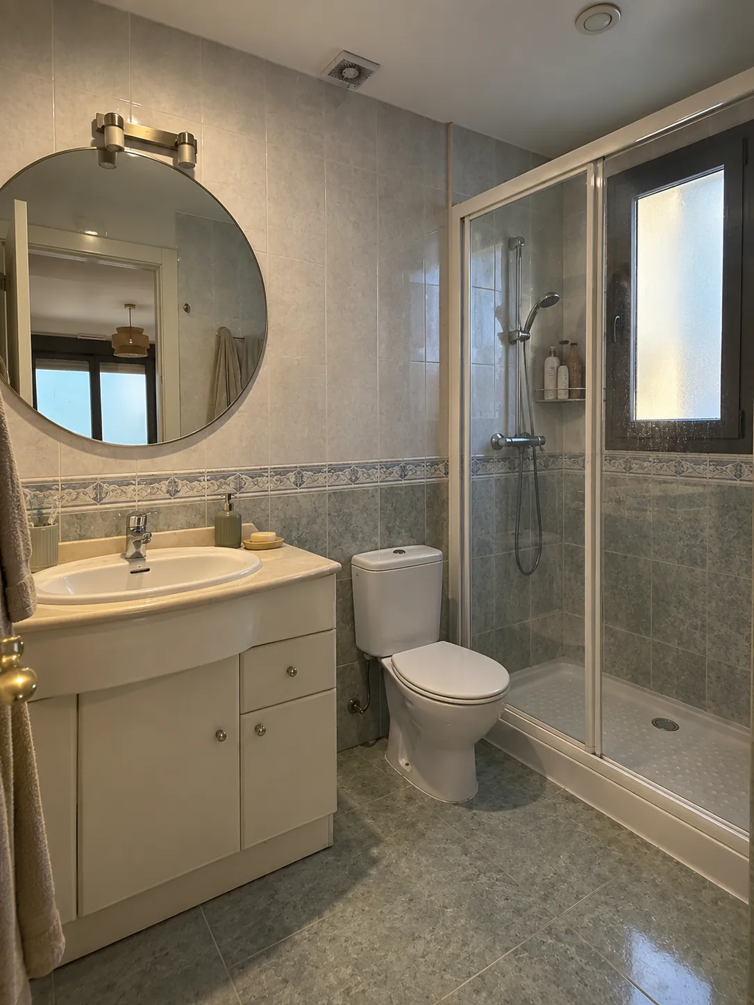 Baño en Pozuelo antes de la reforma: alicatado verde con cenefa, mueble de lavabo e inodoro de tanque