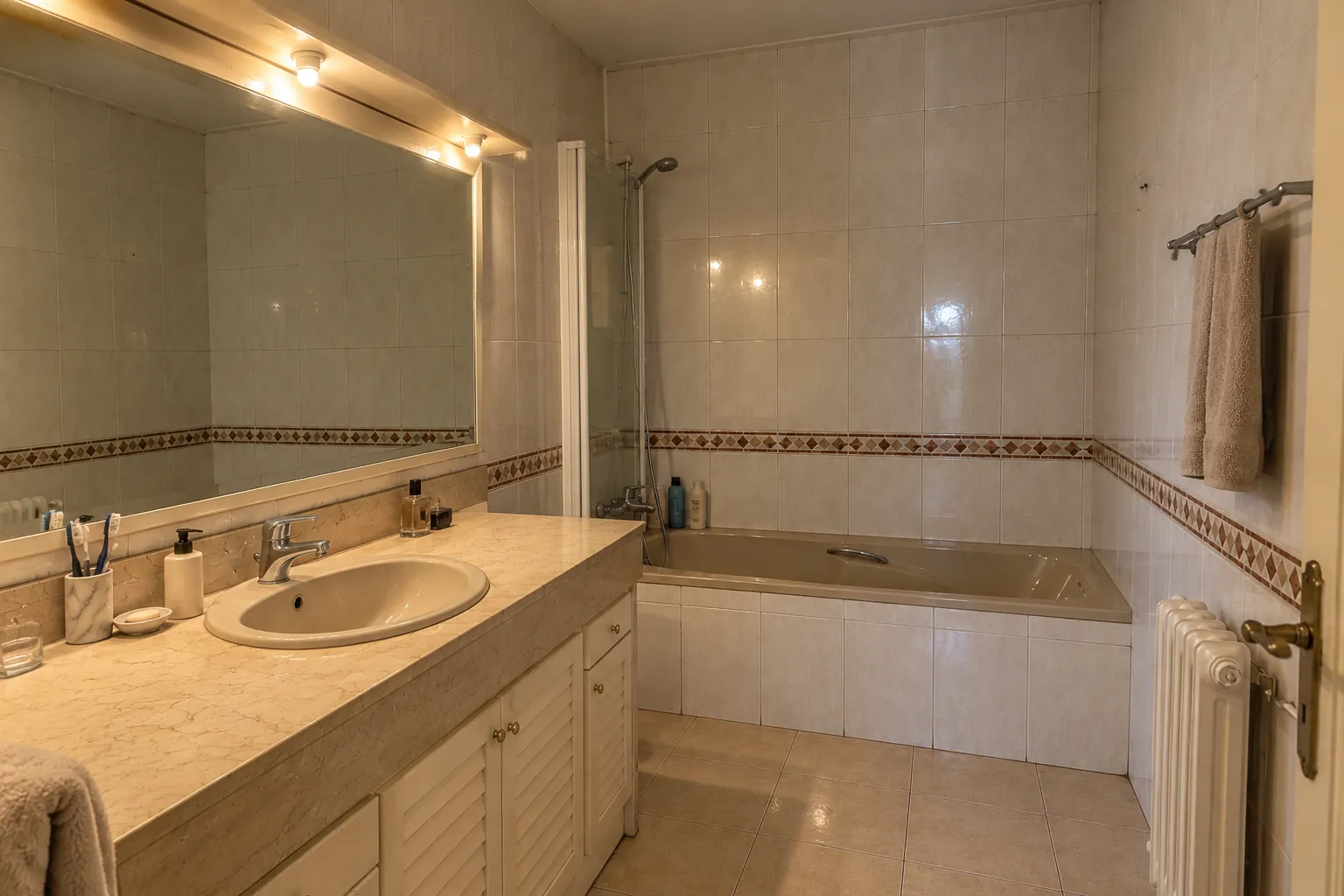 El baño antes: bañera empotrada con mampara abatible, encimera de mármol con lavabo y alicatado con cenefa